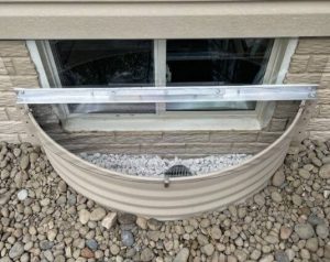 Sloped cover on a metal semi-circle well. The basement window is protected by a plastic panel.